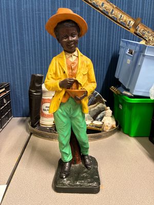 une statue représentant un homme vêtu d'une veste jaune et d'un chapeau, posée sur une table
