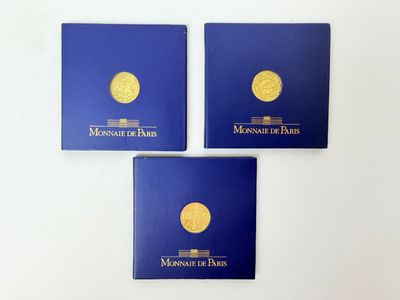 trois livres bleus ornés de pièces d'or, posés sur une surface blanche