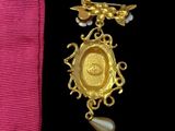 a gold medal and a pearl brooch on a pink ribbon