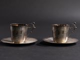 deux tasses et soucoupes en argent posées sur une table