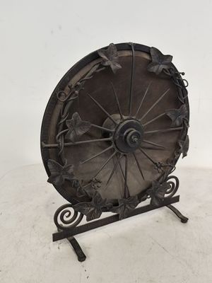 roue en fer forgé posée sur un socle, sur fond blanc avec un mur blanc