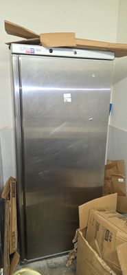 a silver refrigerator in the corner of a room with boxes on the floor