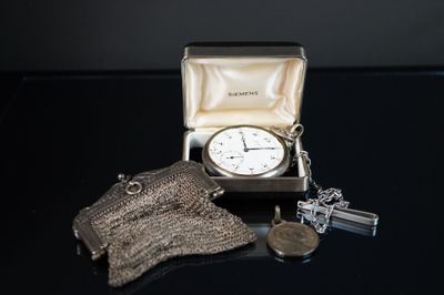 a silver clock in a silver case with a chain around it