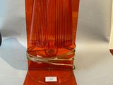 an orange glass vase with a gold base on a white background