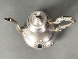 a silver tea pot with a handle on a table