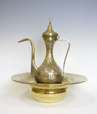 une théière en laiton ancien posée sur une assiette dorée à fond blanc