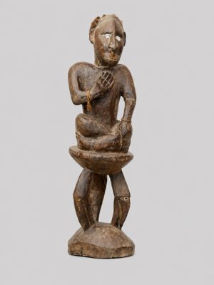 une petite statue en bois représentant un homme tenant un bol
