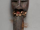 a wooden mask hanging on a wall with a chain around it