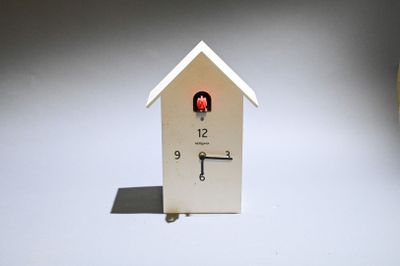 a white clock with a red light in the shape of a house
