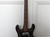 une guitare électrique posée sur un parquet, près d'un mur blanc
