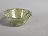 green glass bowl sitting on top of a table next to a white wall