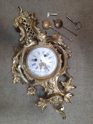 une horloge en or posée par terre à côté d'une paire de ciseaux
