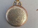 a gold pocket watch on a white surface next to a pair of scissors