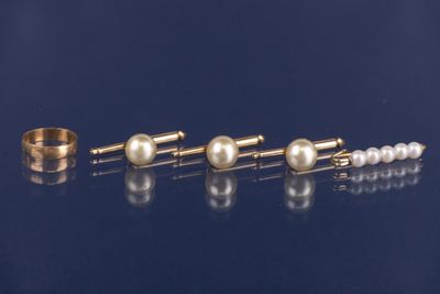 trois paires de boucles d'oreilles en perles et une bague en or posées sur un fond bleu