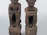 pair of carved wooden figures of two men sitting on stools