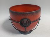 a red bowl with a black handle on a white surface