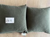deux coussins verts, avec une étiquette de prix, posés sur un plancher en bois