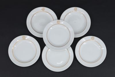 six assiettes blanches aux bords dorés reposent sur une surface noire