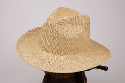 une image représentant un chapeau de paille posé sur un support en bois
