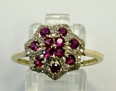 un gros plan d'une bague sertie d'un diamant et d'un rubis posée sur une surface transparente