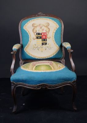 une vieille chaise dont l'assise est recouverte d'un tissu bleu et sur laquelle figure un blason