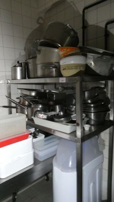 pots and pans are stacked on top of a metal shelf in a kitchen