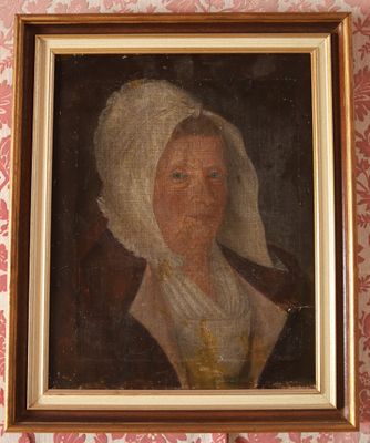 portrait d'une femme coiffée d'un bonnet blanc, dans un cadre doré, accroché à un mur tapissé de papier peint rose