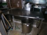 une grande table en inox dans une cuisine, avec une poubelle