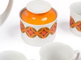 several cups and a teapot are arranged on a white surface