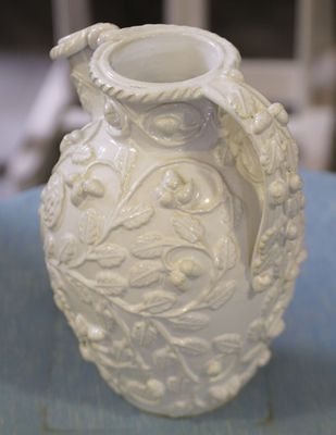 un vase blanc posé sur une table bleue, avec une chaise en arrière-plan