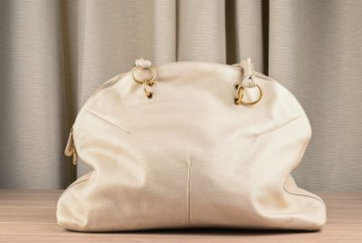 a white purse sitting on a table with a curtain behind it