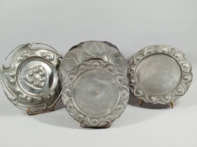 three silver plates with designs on them sitting on a white surface