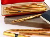 trois stylos et un cahier dans un étui rouge posé sur une surface blanche