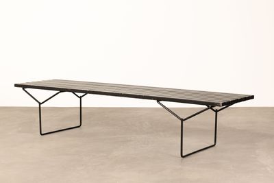 a black bench sitting on top of a cement floor next to a white wall