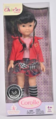 La poupée se trouve dans une boîte, vêtue d'une veste rouge et d'une jupe noire.