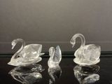 trois figurines de cygnes en verre transparent posées sur une table noire