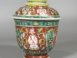 un vase orange, vert et blanc muni d'un couvercle, posé sur un socle