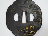 une tsuba en fer ornée de motifs dorés sur fond blanc