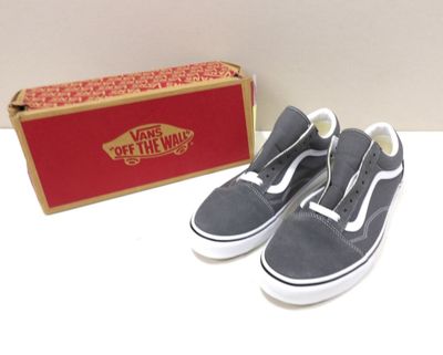 une paire de Vans grises sans lacets à côté d'une boîte contenant des boîtes rouges