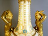 a gold and white vase with two statues on top of it