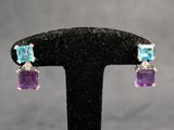 une paire de boucles d'oreilles en cristal violet et bleu, posées sur un socle noir