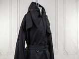 une photo d'un trench-coat noir accroché à un mur blanc
