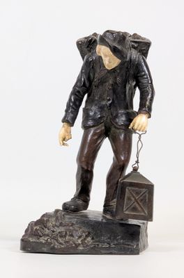 statue représentant un homme avec un sac à dos et une valise, assis sur un rocher