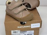 des chaussures de bébé en cuir beige dans une boîte posée sur une surface blanche