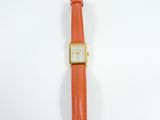 an orange watch with a gold case and a leather strap