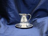 a silver pitcher sitting on a saucer on a blue cloth