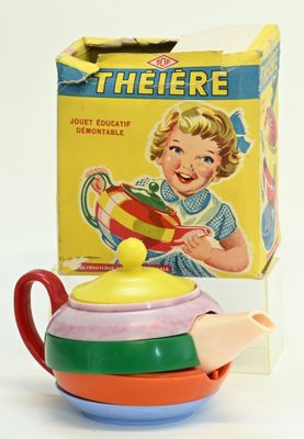 a small teapot with a colorful lid next to a box of tea