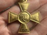 someone is holding a small gold cross with a medal on it