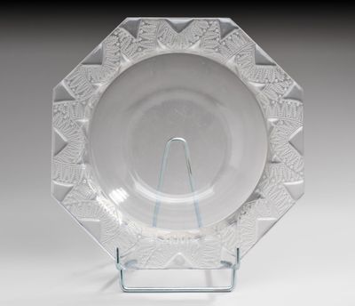 une assiette en verre transparent posée sur un support métallique, sur une table