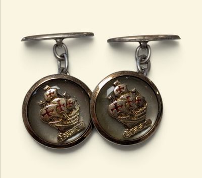 pair of silver cufflinks with a picture of a ship and a crown on them